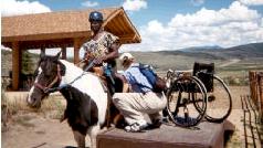 Wheelchair user being secured to horses saddle