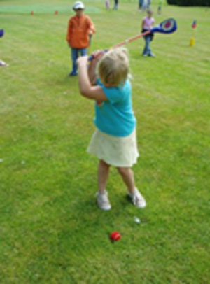 A young girl swings at a golf ball.