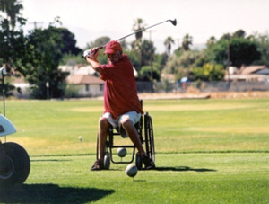 A man using a wheelchair swings at a golf ball.