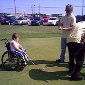 A photo of a young boy seated in a wheelchair playing golf.
