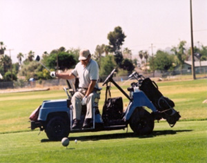 A man seated in a golf cart takes a swing at the ball.