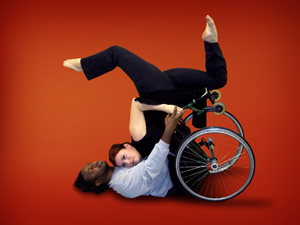 A man that uses a wheelchair is dancing with a woman in a modern dance pose.