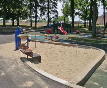This sand play area offers a sand table, a transfer system, and concrete containment edging that users may sit on.