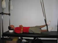 A man is using a pilates machine demonstrates a modified position of the leg springs to accommodate weaker leg muscles