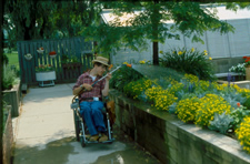 Wheelchair user watering plants in raised bed with a long stick-like hose attachment