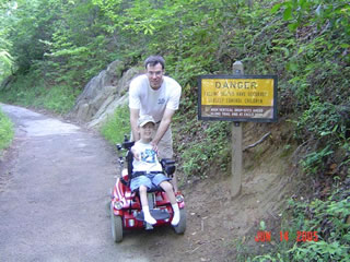 A young boy in a wheelchair and his father pose for a picture at the Smokie Mountains.